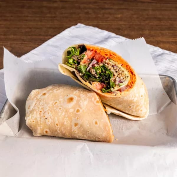 Two halves of a healthy wrap, filled with greens, shredded carrots, and grains, on white paper.