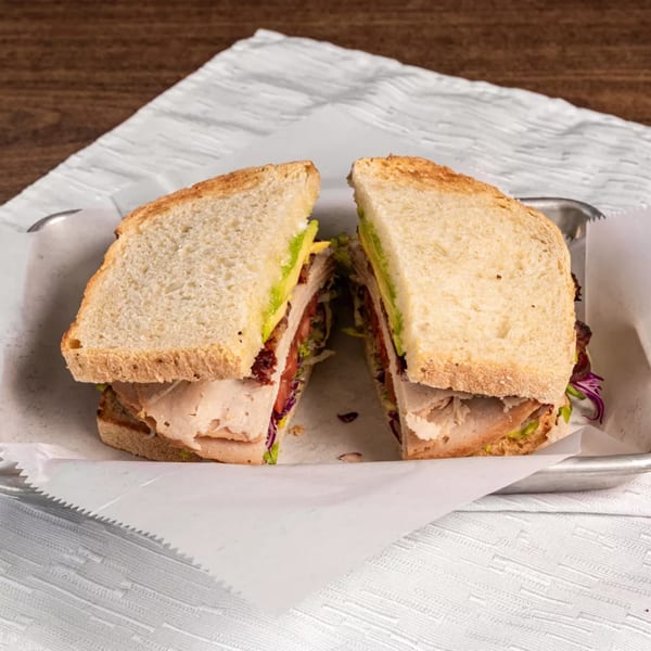 A healthy turkey and avocado sandwich, cut in half, served on a metal tray with white paper.