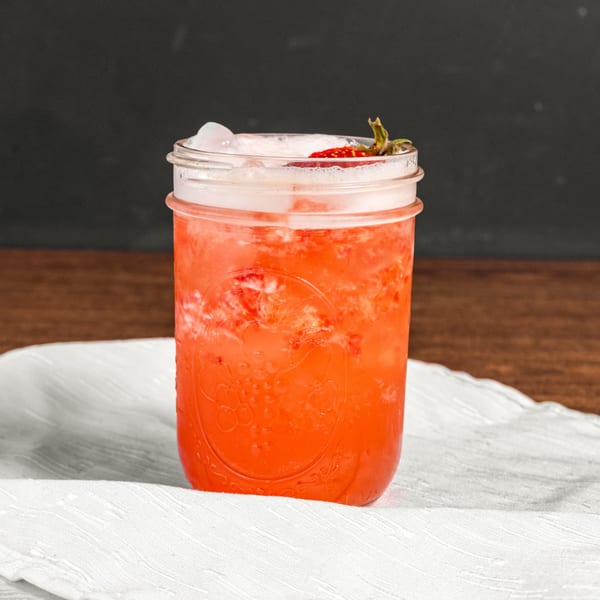 A vibrant red strawberry drink with ice and a strawberry garnish in a mason jar.