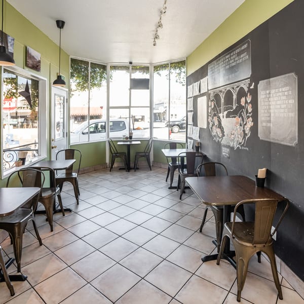 Interior of The Healthy Habit restaurant with light green walls, chalkboard art, and empty tables by large windows.