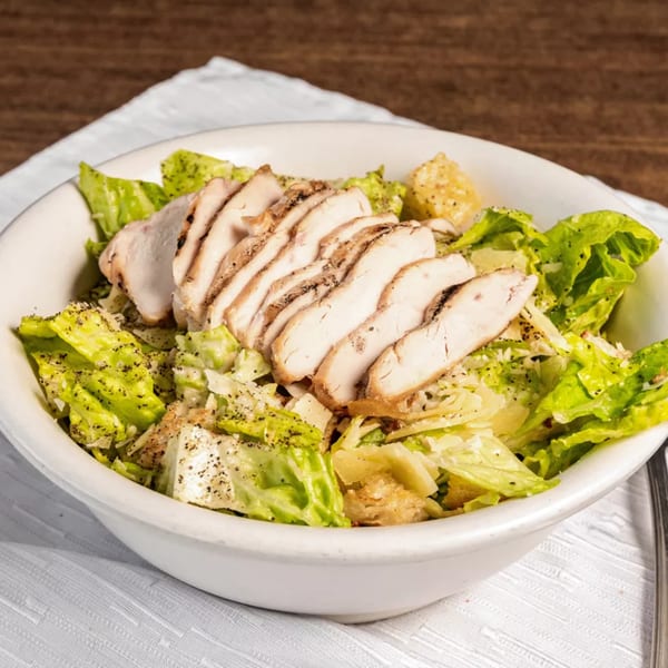 Grilled chicken Caesar salad with fresh romaine, croutons, and parmesan cheese in a white bowl.