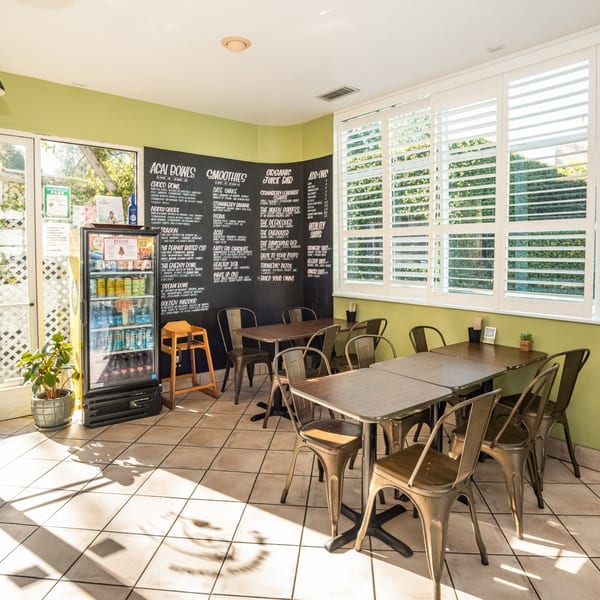 The Healthy Habit's bright dining area with tables, chairs, a drink cooler, and a menu board.