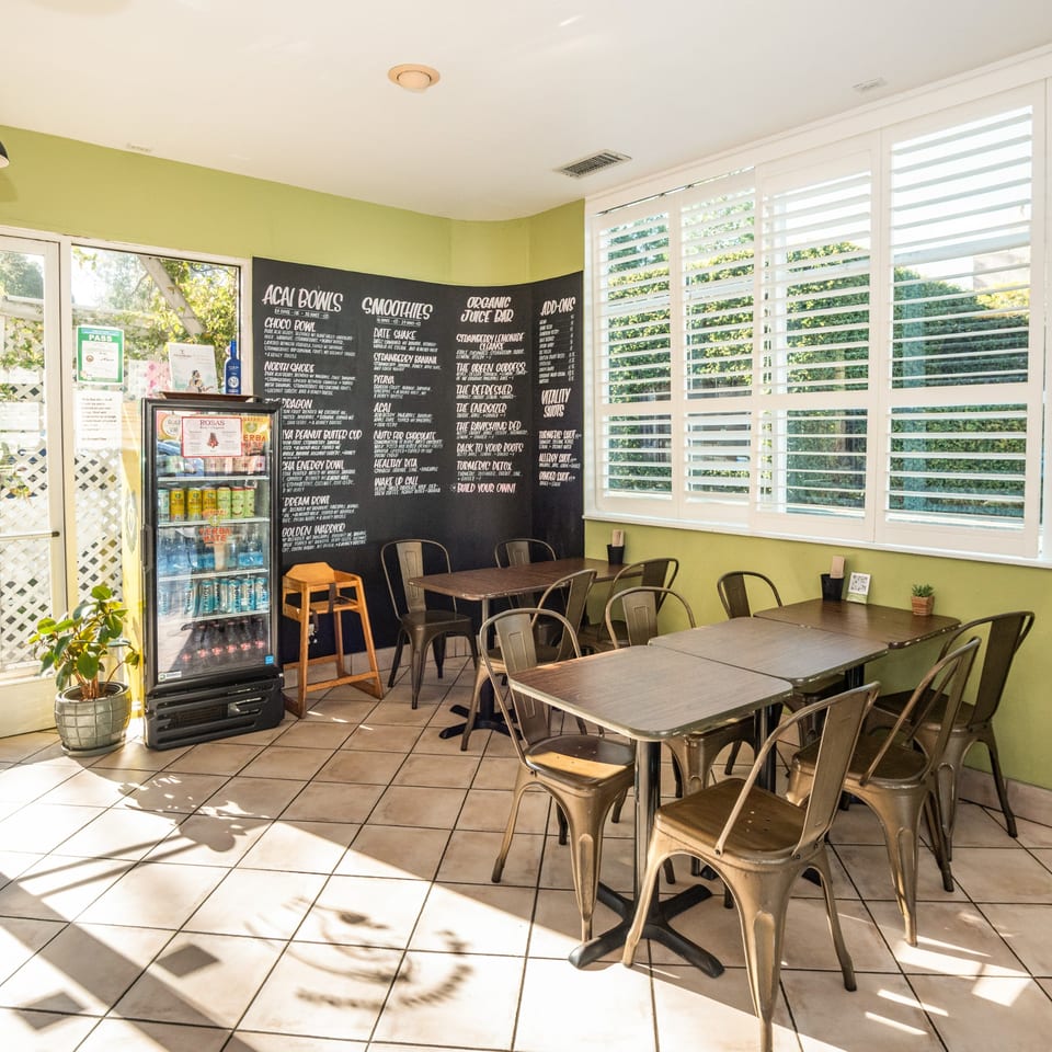 The Healthy Habit's bright dining area with tables, chairs, a drink cooler, and a menu board.