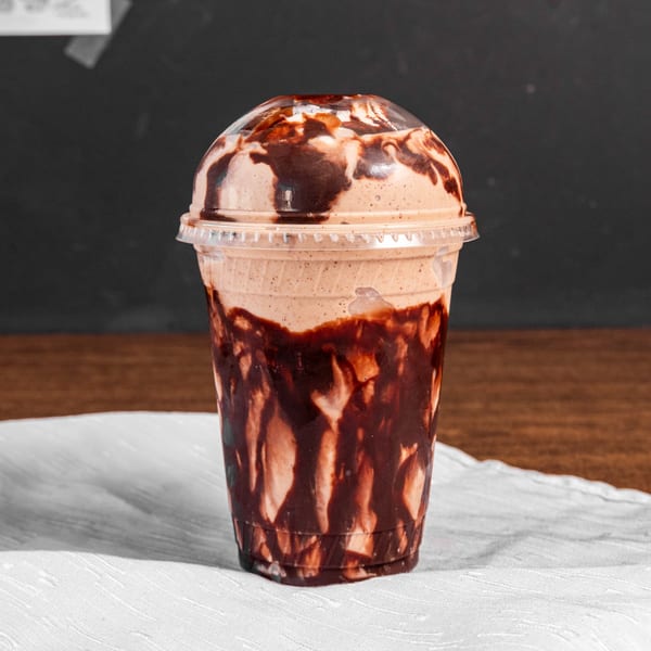 A chocolate smoothie with chocolate syrup drizzled inside a clear plastic cup.