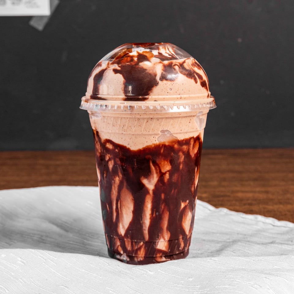 A chocolate smoothie with chocolate syrup drizzled inside a clear plastic cup.