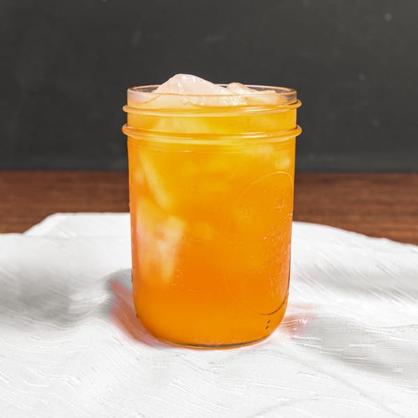 A vibrant orange drink with ice in a mason jar, condensation visible, on a white tablecloth.